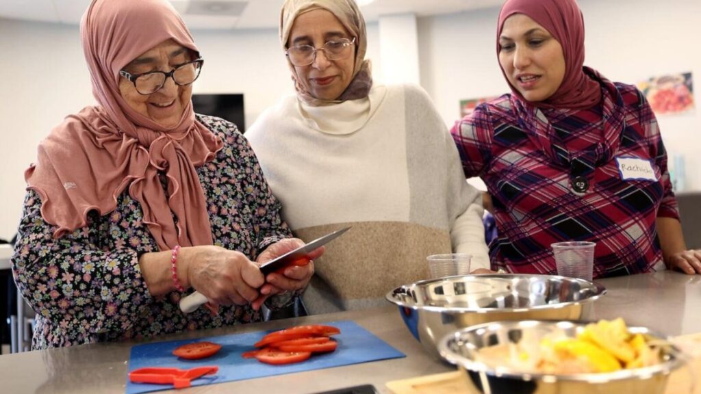 Drie vrouwen snijden samen tomaten in een keuken tijdens Gezond en Fit